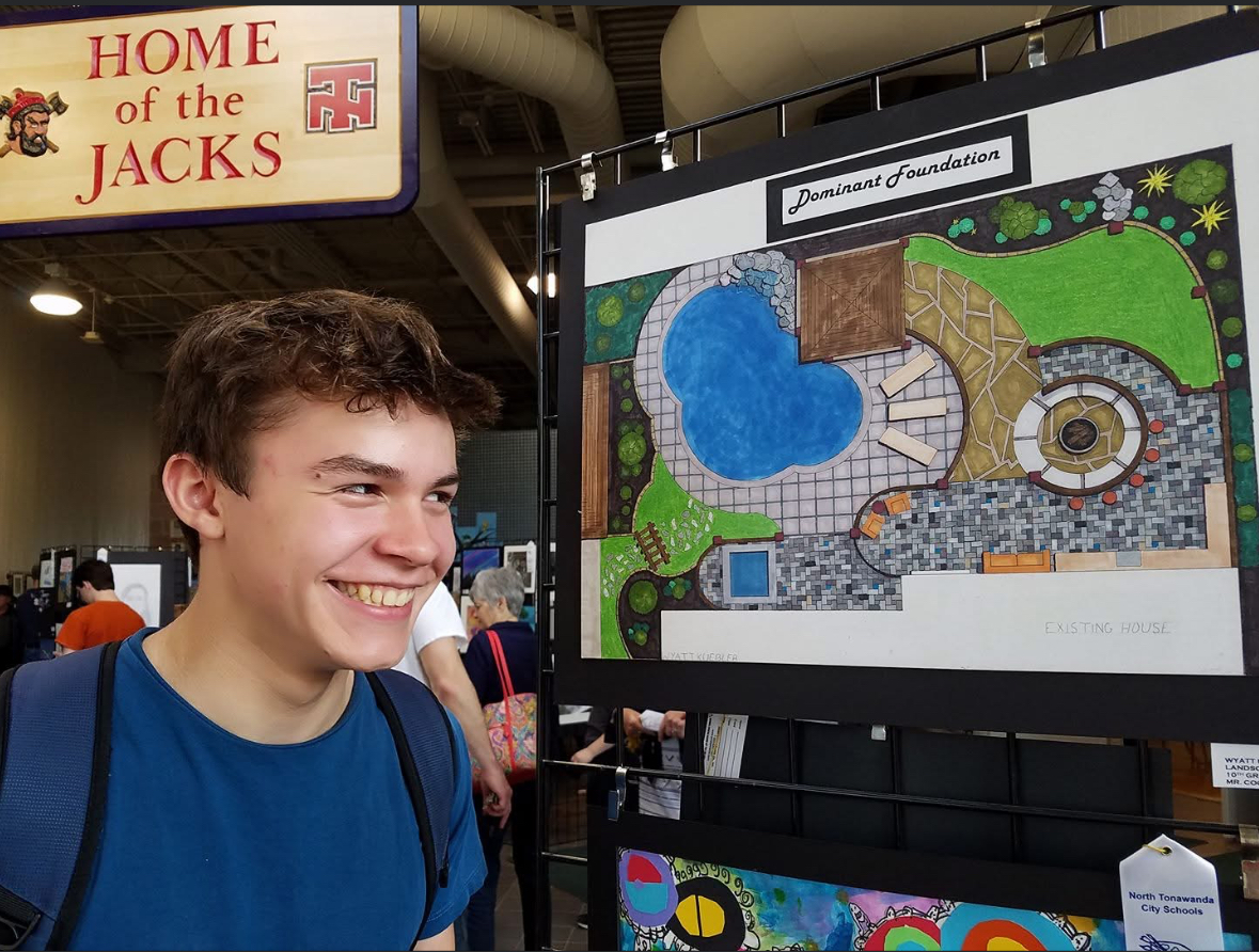 Student standing beside visual arts work at a school art show